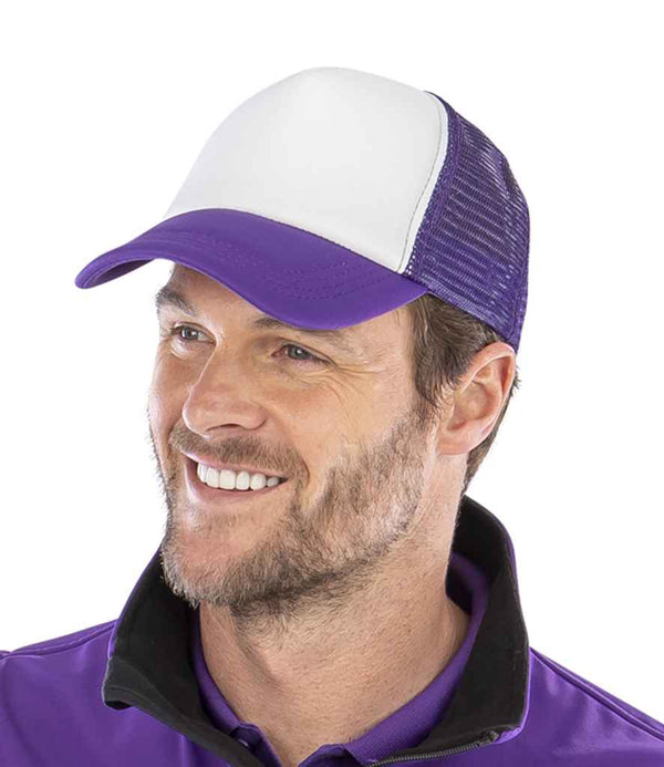 A man with light facial hair smiles while wearing the Result Core 1/2 Mesh Truckers Cap by Result Headwear, featuring a white and purple design with a recycled PE peak, paired with a purple shirt with a black collar.