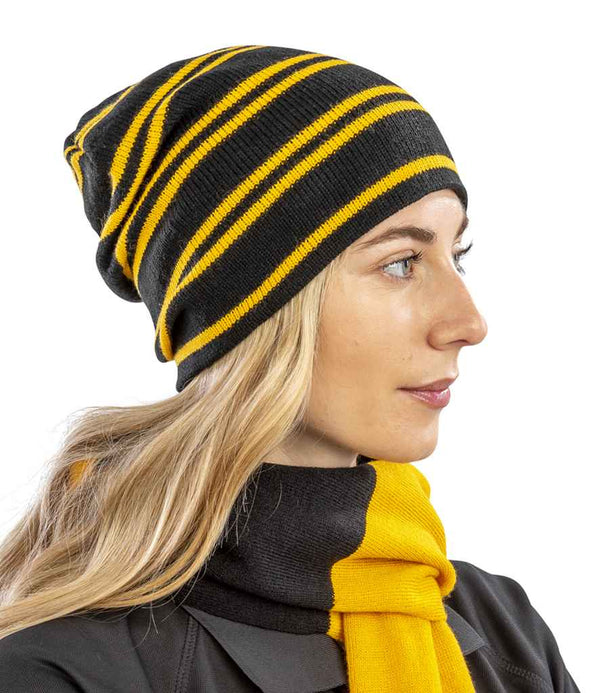 A woman with long blonde hair wears the Result Team Reversible Beanie by Result Winter Essentials, paired with a matching striped scarf. She faces right against a plain white background.