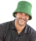 A man with a beard and mustache smiles at the camera, wearing a Result Recycled Result Core Recycled Bound Edge Bucket Hat in green, featuring an 8-stitch line brim and stitched eyelets, paired with a black collared shirt against a white background.