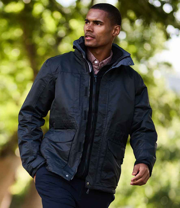 A man wearing the Regatta Professional Benson III 3-in-1 Breathable Jacket walks outdoors in front of blurred greenery, paired with a light shirt and dark pants.