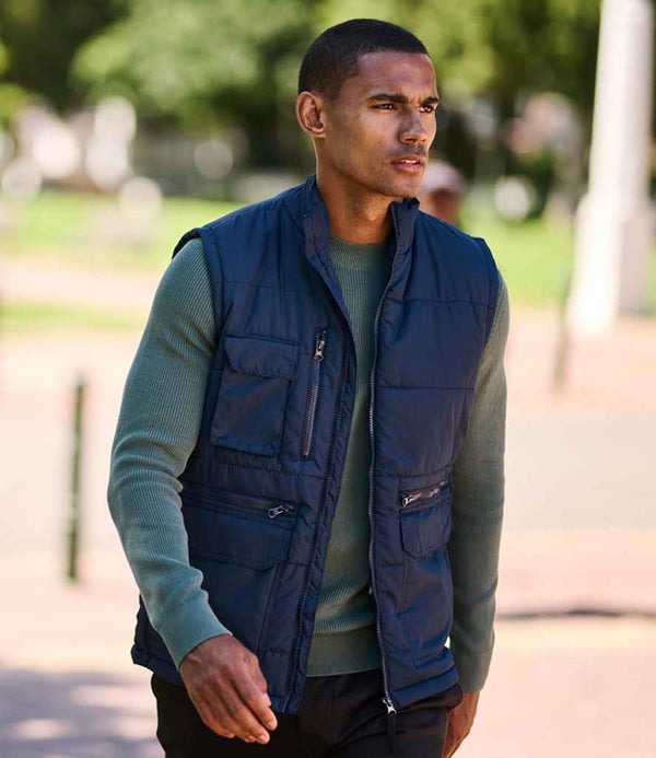 A man in a green long-sleeve shirt and a navy blue Regatta Steller Bodywarmer by Regatta Professional, featuring Recycled Thermo-Guard insulation, walks outdoors with blurred greenery and pavement in the background.