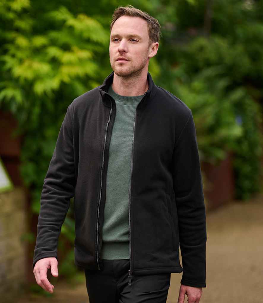 A man with short hair walks outdoors on a path, wearing the Regatta Honestly Made Recycled Micro Fleece Jacket over a green sweater, with greenery in the background.