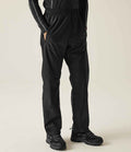 A person wears Regatta Pro Packaway Waterproof Breathable Overtrousers by Regatta Professional and black hiking shoes, standing against a plain light background.