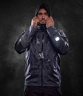 A person adjusts the hood of the Regatta X-Pro Beacon Brite Light Waterproof Shell Jacket by Regatta Professional, standing against a dark background with water droplets. A reflective sleeve detail enhances visibility in low light.