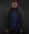A man faces forward wearing the Regatta X-Pro Evader III 3-in-1 Jacket by Regatta Professional, a black waterproof coat with blue zippers and trim over a black recycled polyester padded layer, set against a plain dark background.