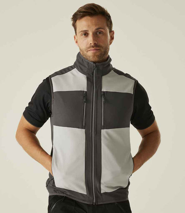 A man faces forward with his hands in his pockets, wearing a short-sleeved black shirt and the Regatta E-Volve Unisex Two Layer Soft Shell Bodywarmer by Regatta Professional. The background is plain and light-colored.