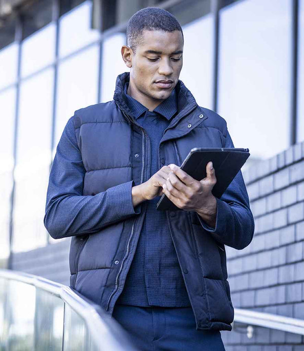 A man wearing the Regatta Professional Northdale Insulated Bodywarmer stands outdoors by a glass building, using a tablet.