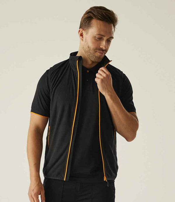A man stands against a neutral background, wearing the Regatta Professional Regatta Navigate Fleece Bodywarmer over a black short-sleeve shirt. He looks down while holding the unzipped vest near his collar, showing its orange zipper detail.