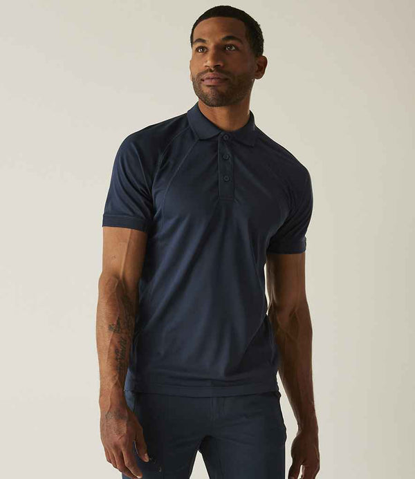 A man with a tattoo on his left forearm stands against a light background wearing the Regatta Professional Regatta Coolweave Piqué Polo Shirt in dark blue. The short-sleeve polo is made from quick-dry wicking performance fabric.