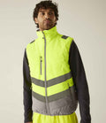 A man wearing a Regatta High Visibility Two Tone Thermal Baffle Bodywarmer, a water repellent, high-visibility yellow vest with gray reflective stripes, stands facing forward against a plain light background.
