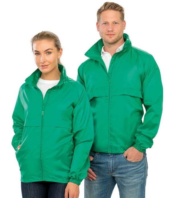 A woman and a man stand side by side, both facing forward in casual outfits and wearing matching green Result Core Windcheater jackets from Result Core. The woman has her hands in her pockets, while the man has his left hand in his pocket.