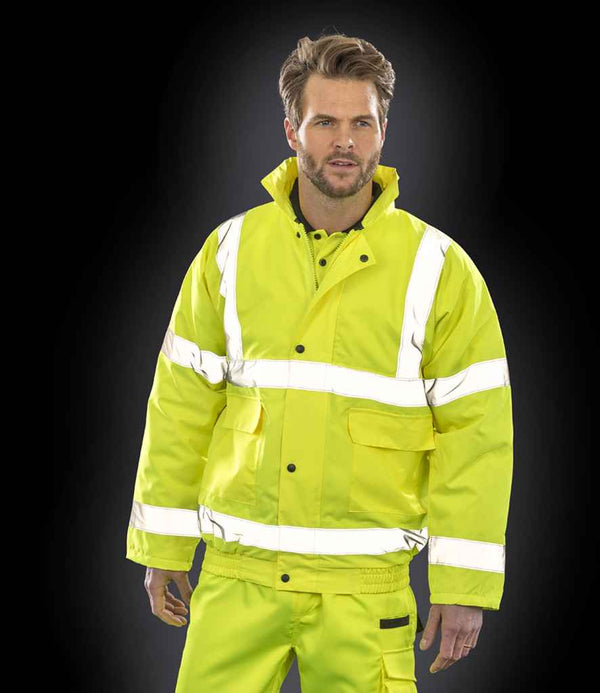 A person wears the Result Core Hi-Vis Winter Blouson Jacket by Result Core, featuring high-visibility yellow fabric and reflective bands, standing against a black background.