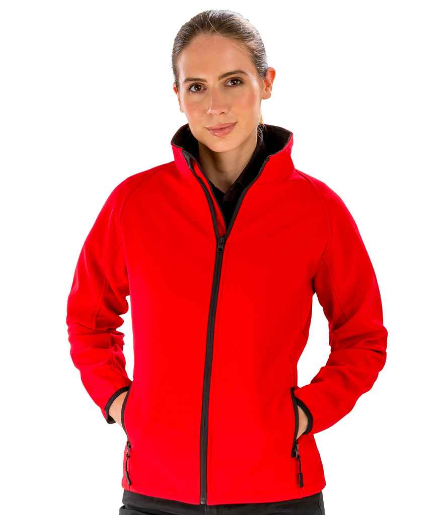 A person wears the Result Core Ladies Printable Soft Shell Jacket by Result Core in bright red with black trim, hands in front pockets, standing against a plain white background.