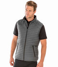A man models the Result Recycled Thermoquilt Gilet—a gray, quilted, showerproof vest with Repreve recycled padding—over a black short-sleeve polo, posed against a plain white background and looking slightly to his right.