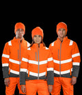 Three people face forward, wearing Result Safe-Guard Ladies Soft Safety Jackets by Result Safe-Guard, certified to EN ISO 20471, in orange and gray with white reflective stripes, plus matching orange pants and beanies.