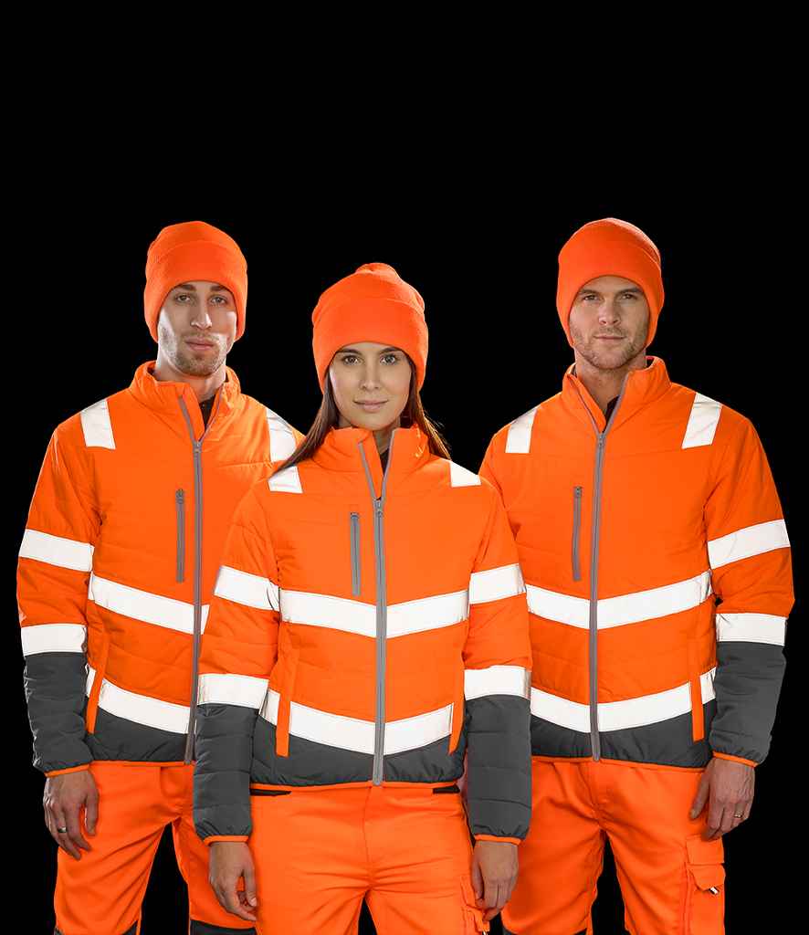 Three people face forward, wearing Result Safe-Guard Ladies Soft Safety Jackets by Result Safe-Guard, certified to EN ISO 20471, in orange and gray with white reflective stripes, plus matching orange pants and beanies.
