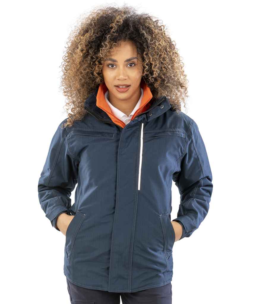 A person with curly hair wears the Result Work-Guard Denim Texture Rugged Jacket—a dark blue, breathable, windproof jacket with zipper, hood, side pockets, and white chest pocket detailing—against a plain white background.