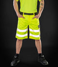 A person stands with hands in pockets, wearing a neon yellow shirt and Result Safe-Guard Hi-Vis Cargo Shorts featuring EN ISO 20471 reflective stripes—perfect for high-visibility workwear—with black shoes and socks, set against a black background. Face not visible.