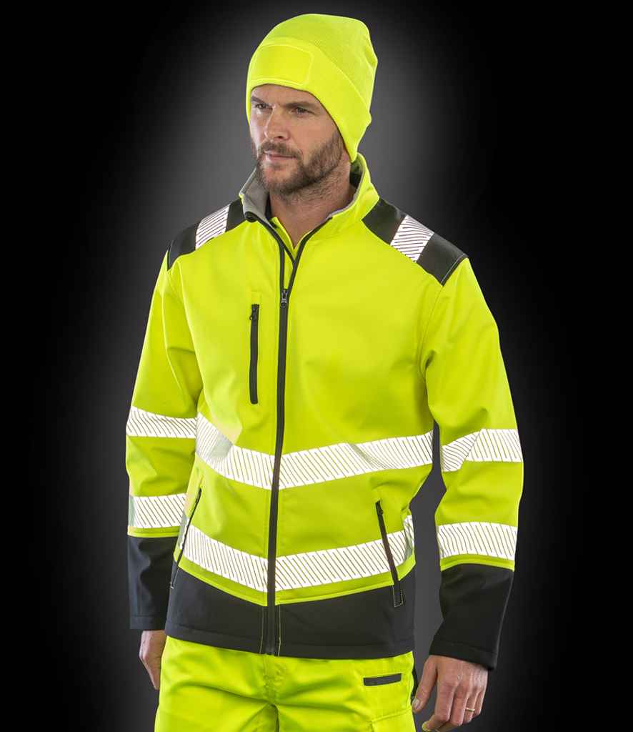 A man in a neon yellow Result Safe-Guard Printable Ripstop Safety Soft Shell Jacket with reflective stripes, matching pants, and a neon yellow beanie stands against a black background.