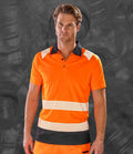 A man wearing the Result Recycled Safety Polo Shirt with white reflective bands, by Result Recycled, stands in front of a dark, textured background.