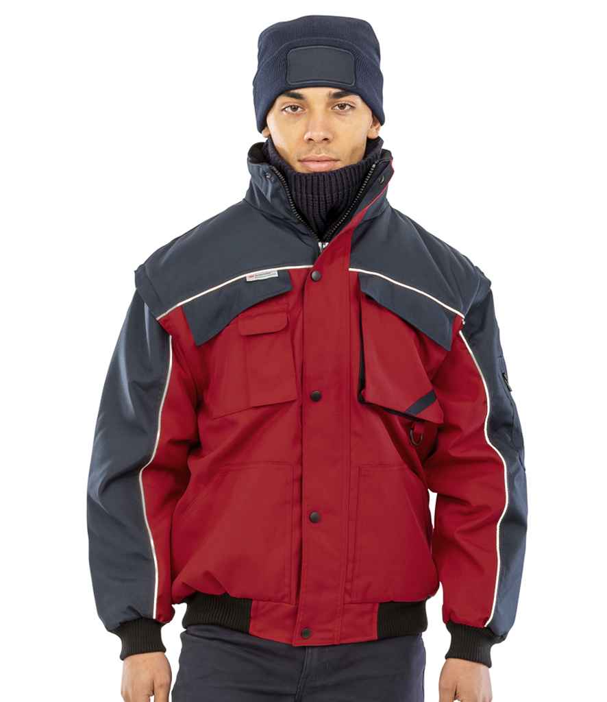 A person wearing a navy blue beanie and the Result Work-Guard Zip Sleeve Heavy Duty Jacket by Result Work-Guard, featuring red and navy colors, multiple pockets, and reflective piping, stands against a plain white background.