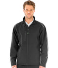 A man faces forward in a Result Recycled Three Layer Printable Soft Shell Jacket by Result Recycled—black, zip-up, waterproof with a high collar and chest pocket, made from recycled polyester—worn over a white collared shirt against a white background.