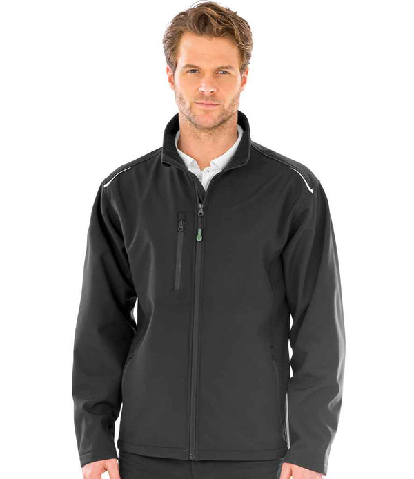 A man faces forward in a Result Recycled Three Layer Printable Soft Shell Jacket by Result Recycled—black, zip-up, waterproof with a high collar and chest pocket, made from recycled polyester—worn over a white collared shirt against a white background.