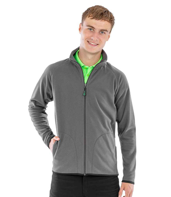 A young man faces forward, smiling, with one hand in his pocket, wearing the Result Recycled Micro Fleece Jacket by Result Recycled over a bright green collared shirt and black pants.
