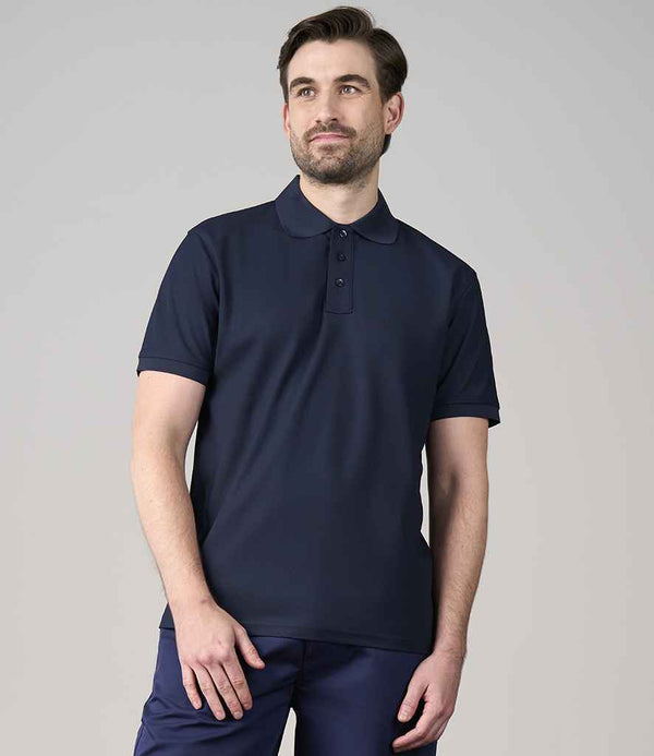 A man with short brown hair and a beard is wearing a dark navy blue Pro RTX Pro Wicking Piqué Polo Shirt by Pro RTX, paired with matching pants, standing against a plain light grey background.