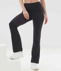 A person models SF Clothing Ladies Flared Leggings—black, high-waisted, soft-touch flared pants—from SF Clothing with white sneakers, posing with one leg bent and the other straight against a light background; upper body is partially out of frame.