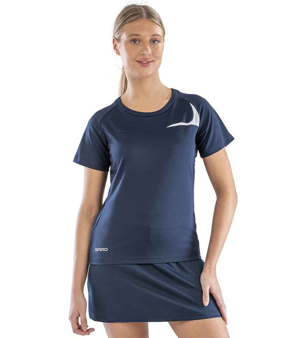 A woman with blonde hair tied back stands facing forward, wearing the Spiro Ladies Dash Training Shirt in navy blue with a white chest logo and SPIRO near the hem. The lightweight shirt by Spiro offers excellent moisture management.