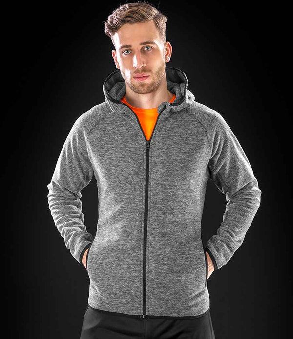 A man faces the camera, wearing a Spiro Micro Fleece Hoodie by Spiro in grey with the hood up over a bright orange shirt. His hands are in his hoodie pockets against a black background.