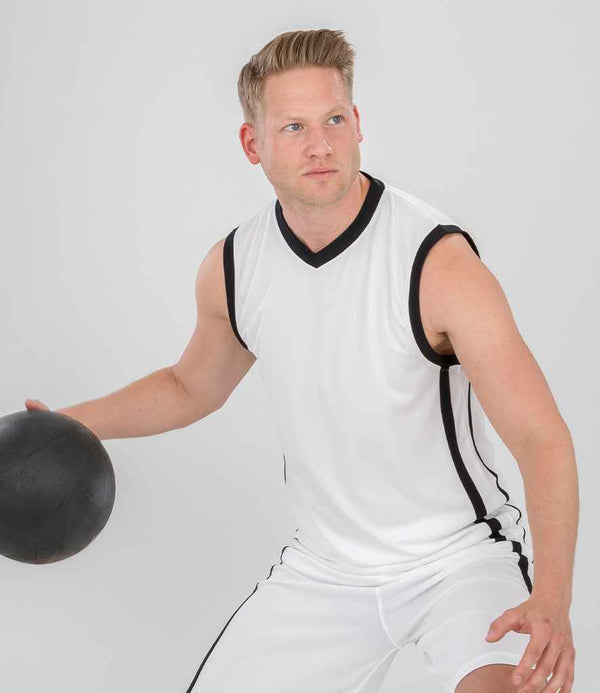 Wearing the Spiro Basketball Top by Spiro, a man in white, breathable sportswear holds a black basketball in one hand, poised for action and looking to the side against a plain light background.