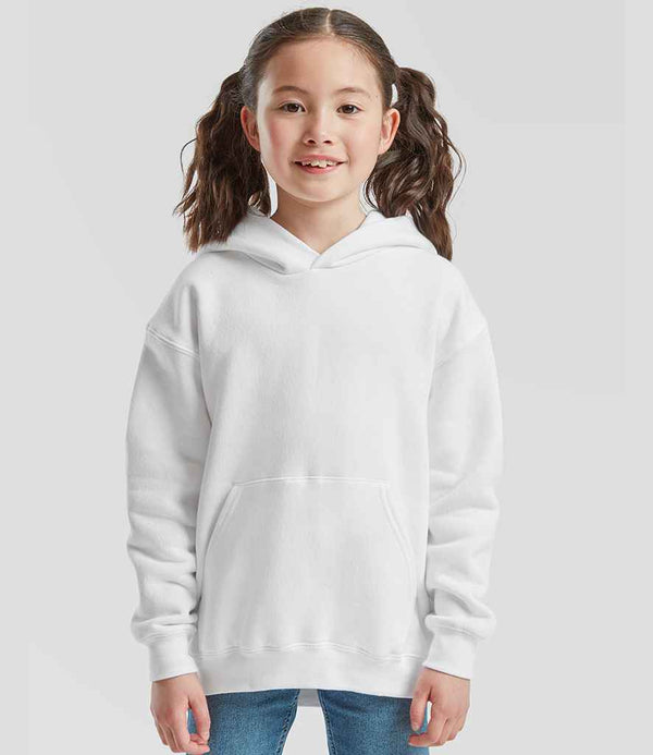 A young girl with brown hair in pigtails is smiling and standing against a grey background, wearing blue jeans and a Fruit of the Loom Kids Premium Hooded Sweatshirt in white.