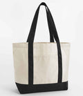 The Westford Mill EarthAware® Organic Varsity Shopper features a beige canvas body, black handles and bottom, cotton shoulder straps, heavyweight fabric, and a front exterior pocket. Displayed against a plain white background.