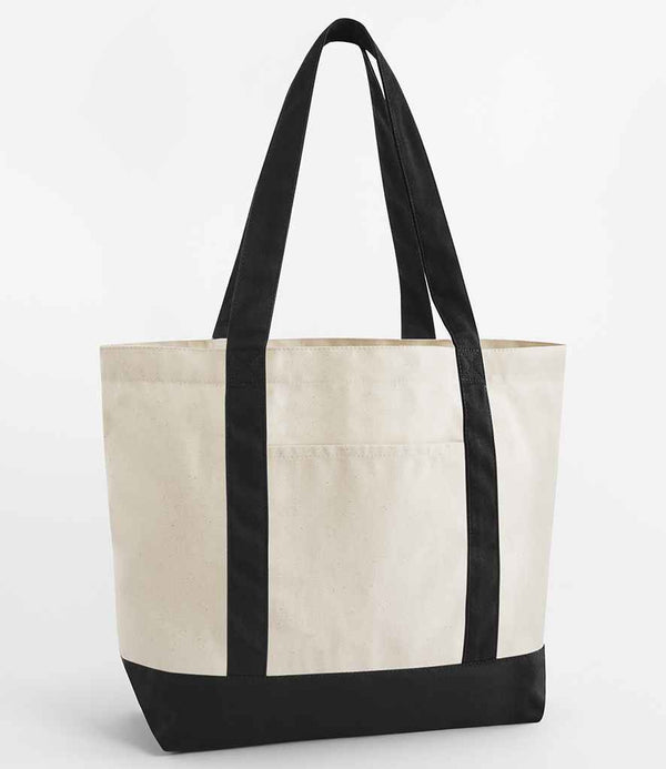 The Westford Mill EarthAware® Organic Varsity Shopper features a beige canvas body, black handles and bottom, cotton shoulder straps, heavyweight fabric, and a front exterior pocket. Displayed against a plain white background.
