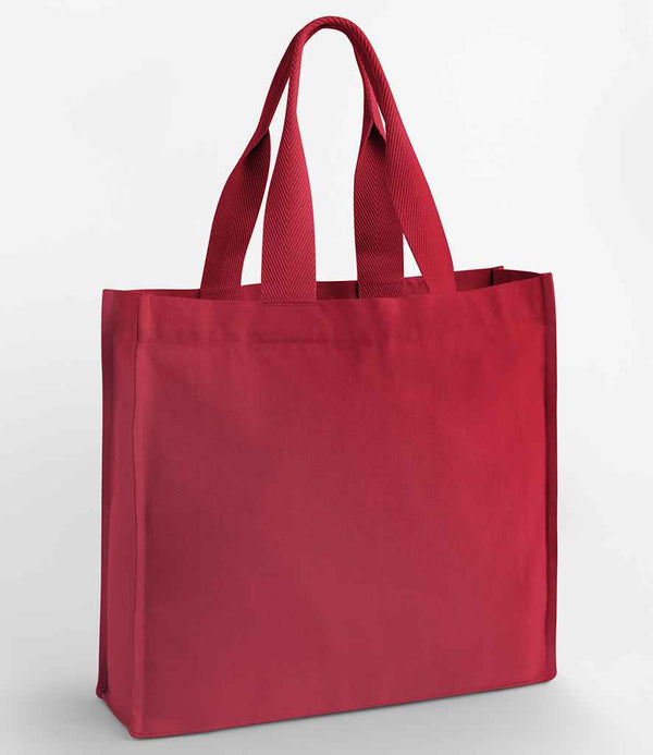The Westford Mill Chevron Handle Shopper, a plain red reusable tote bag by Westford Mill, stands upright against a white background.