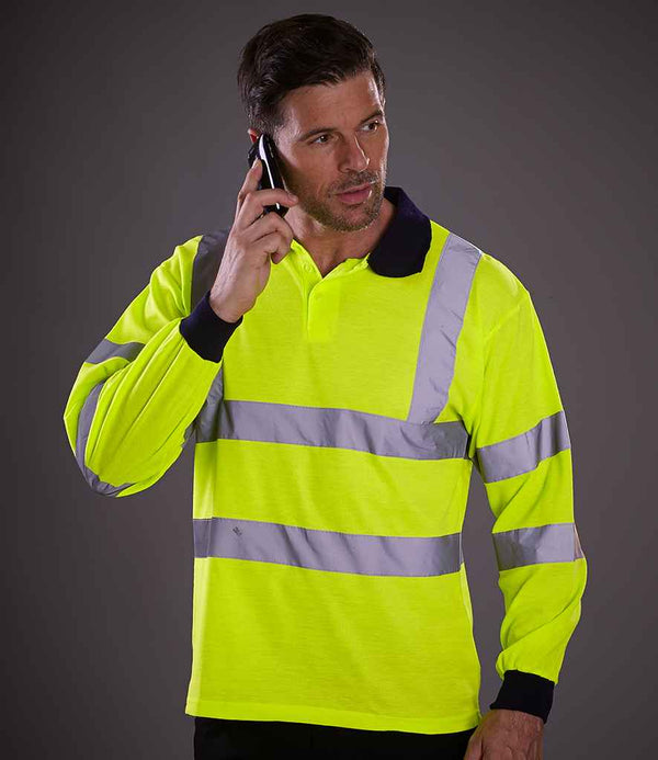 A man wearing a YOKO Yoko Hi-Vis Long Sleeve Polo Shirt with reflective bands and EN ISO 20471 class 3 certification holds a mobile phone to his ear, looking to the side against a plain gray background.