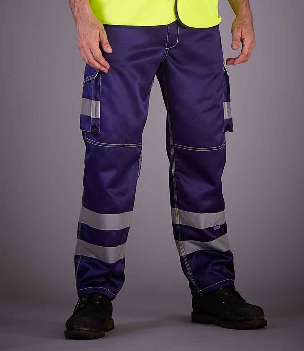 A person stands against a plain background wearing YOKO Hi-Vis Cargo Trousers with knee pad pockets, featuring reflective bands, paired with a yellow high-visibility vest and black work shoes. The face is not visible.